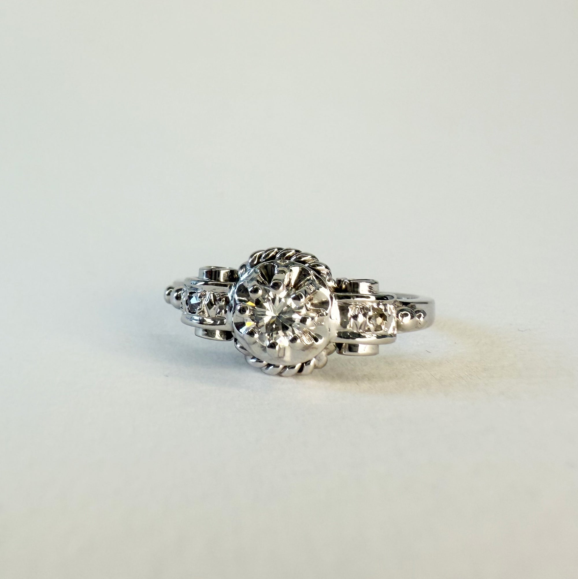 Bague ancienne en or blanc 18 carats ornée d’un diamant taille brillant d’environ 0,1 carat, monture à volutes et torsades inspirée de l’Art Déco, bijou élégant des années 1950.