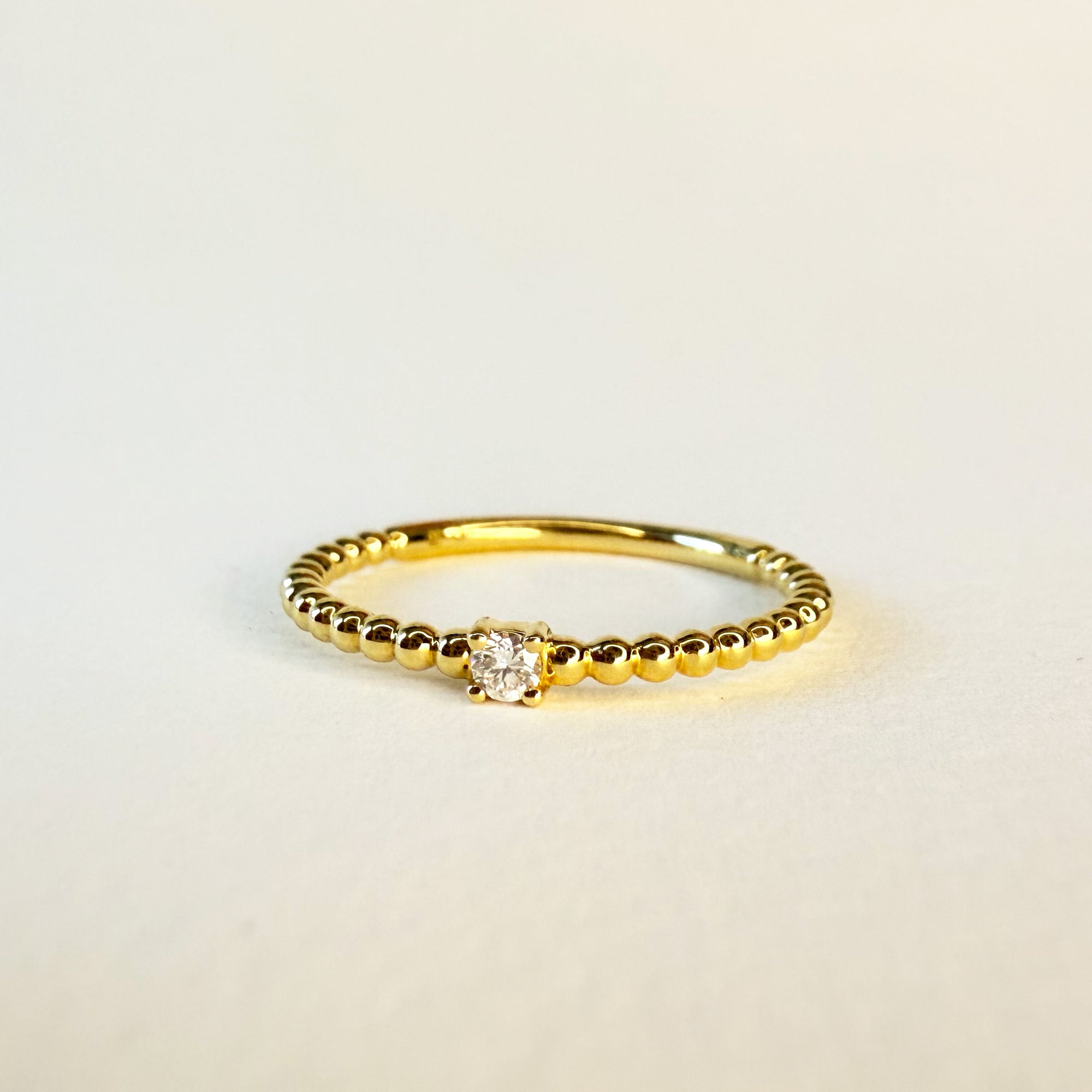 Bague solitaire en or jaune 18 carats ornée d’un diamant en serti griffe sur un anneau perlé, bijou raffiné symbolisant l’unicité et l’élégance intemporelle.