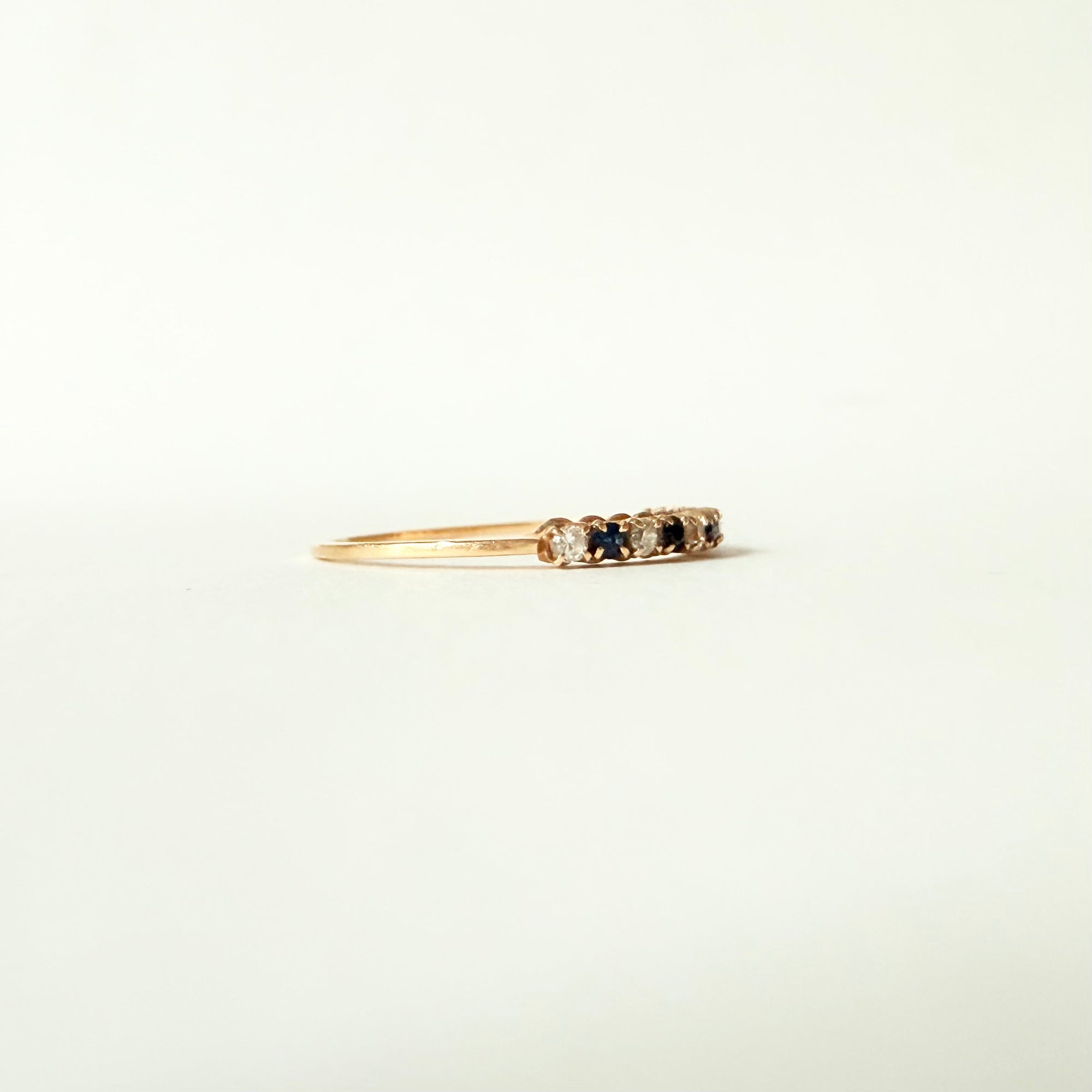 Vue de profil d’une fine bague demi-alliance en or jaune 18 carats sertie de diamants et saphirs
