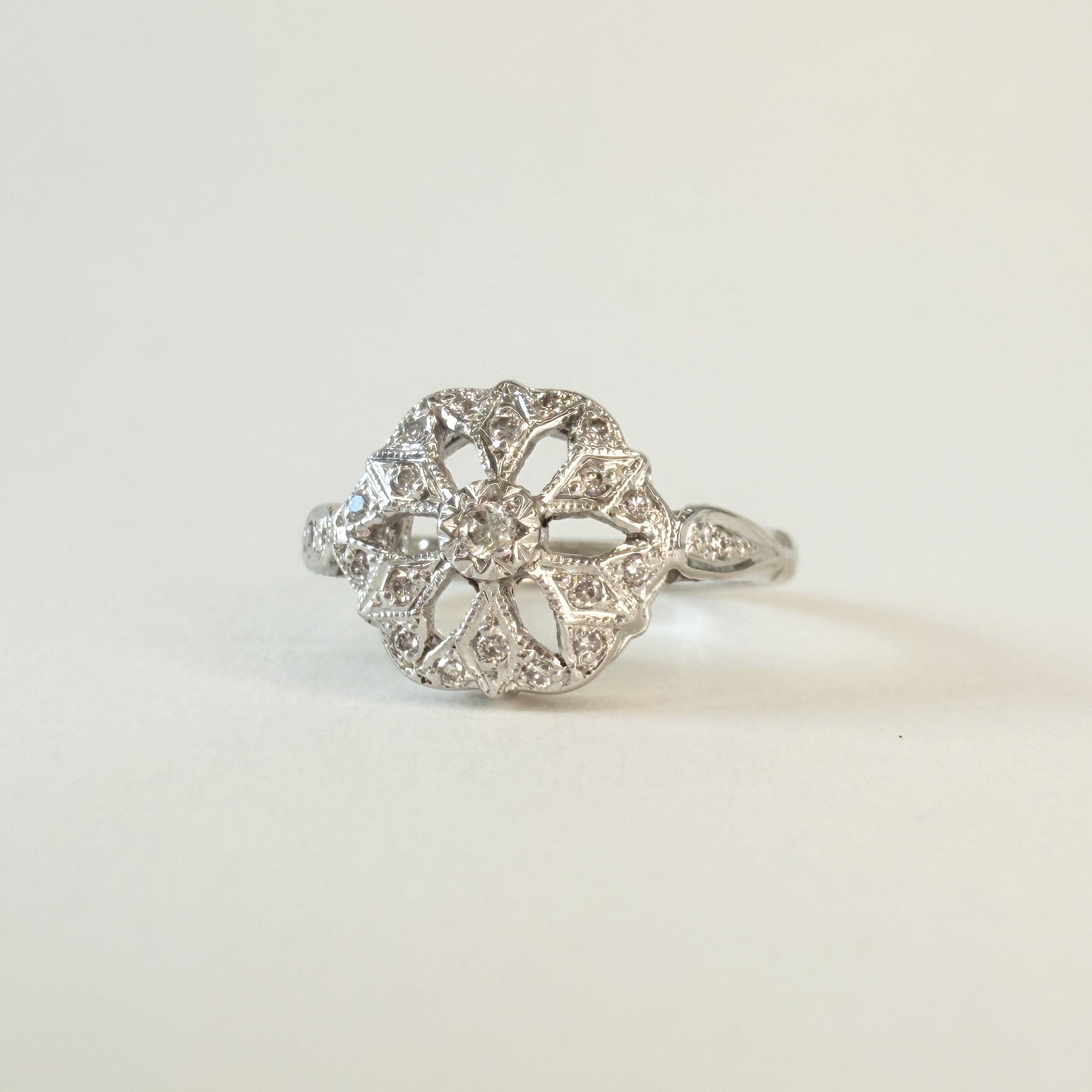 Bague en or gris 14 carats ajourée sertie de diamants taille brillant, motif délicat en forme de fleur ou de flocon, bijou raffiné et lumineux.