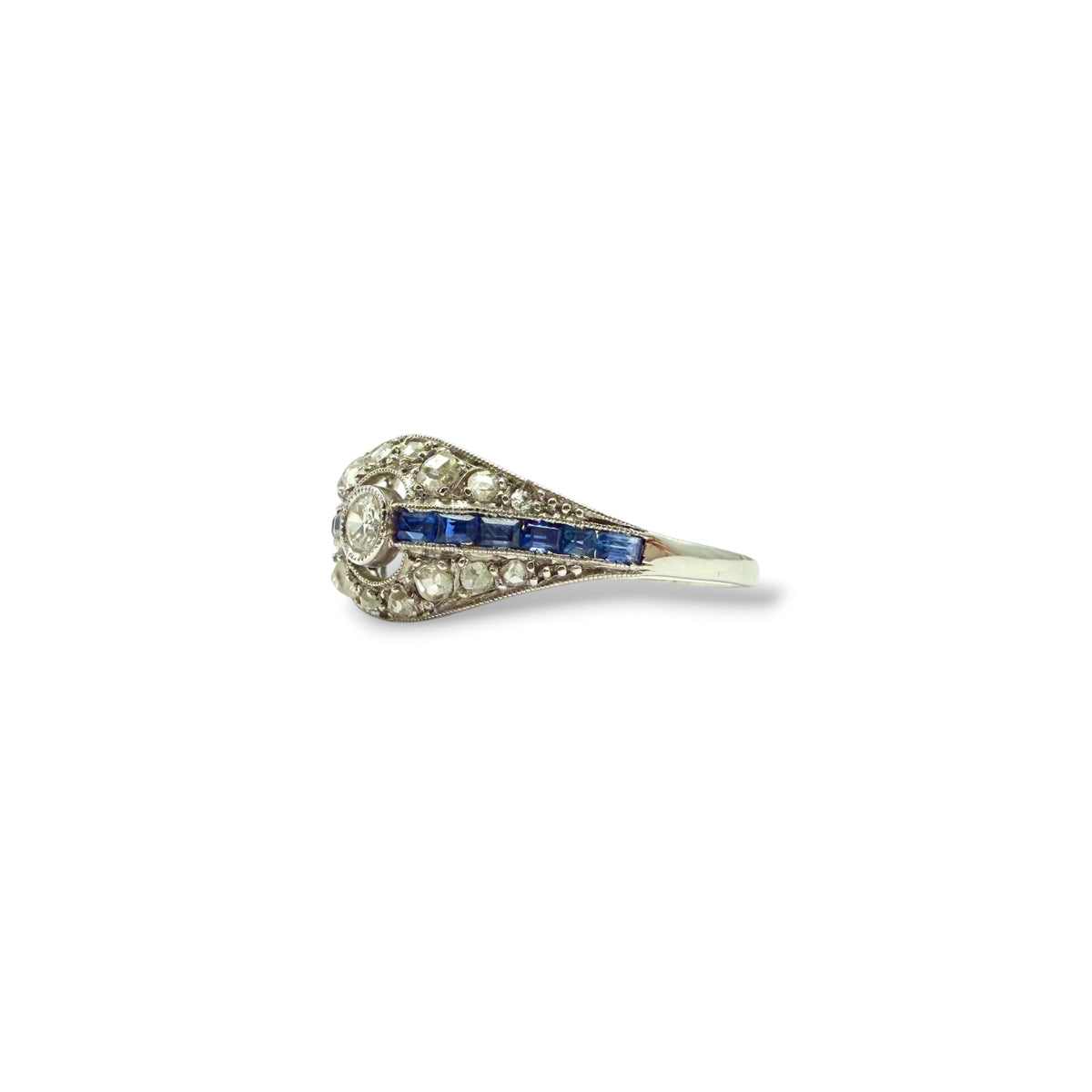 Profil d’une bague ancienne Art Déco en or blanc 18 carats, révélant une monture en dôme ajouré sertie de diamants et de saphirs.