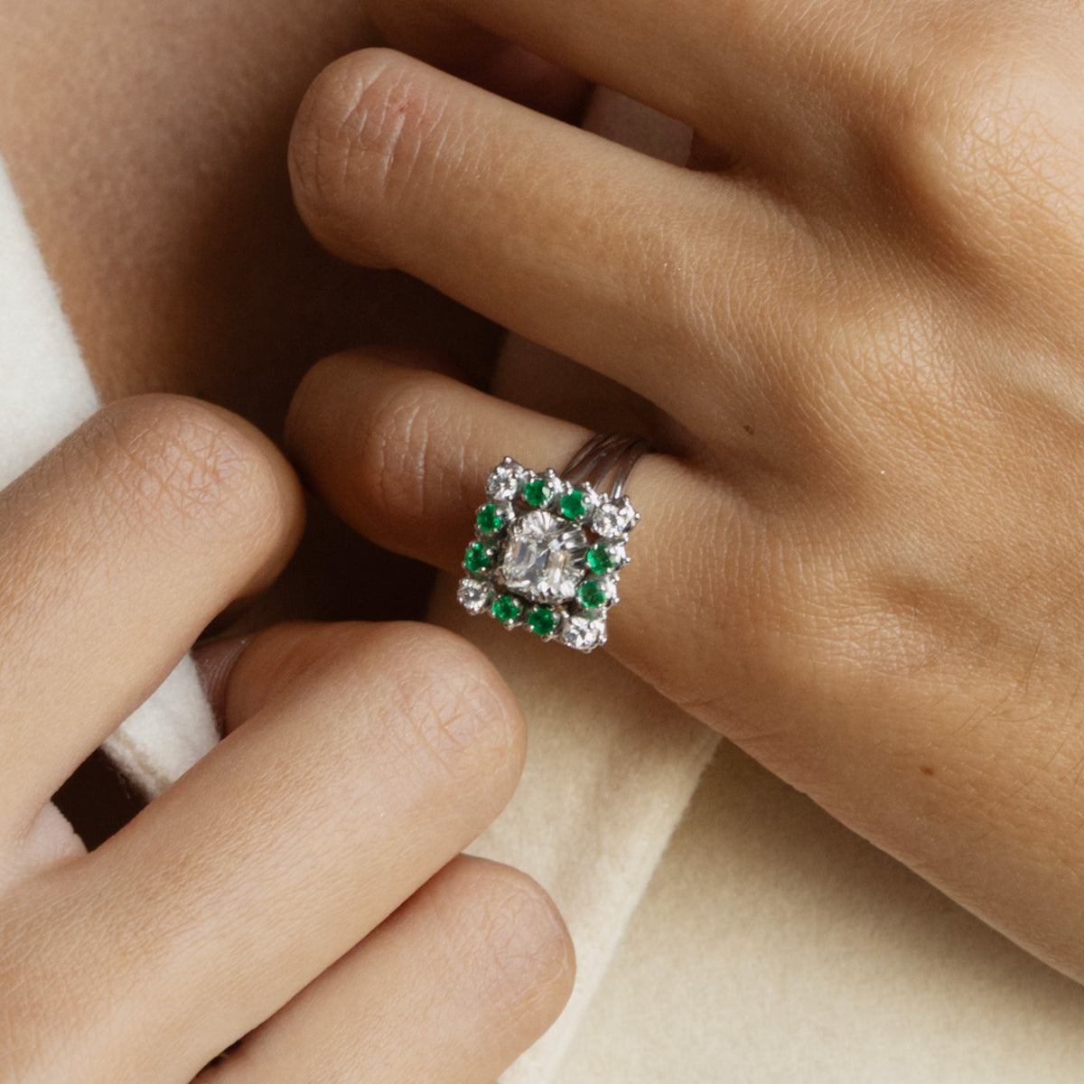 Bague marguerite en or gris 18 carats sertie d'un diamant taille émeraude entouré d'émeraudes et de diamants, vue portée au doigt.