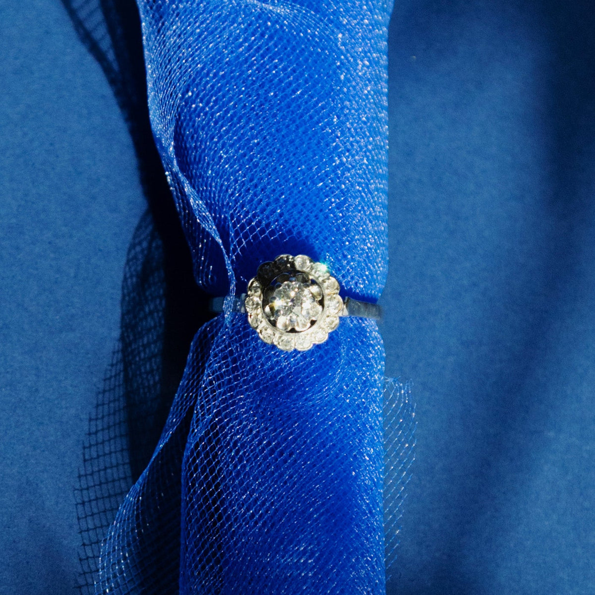 Bague Art déco en platine et or gris 18 carats sertie d'un diamant taille ancienne entouré de diamants, photo sur fond bleu.
