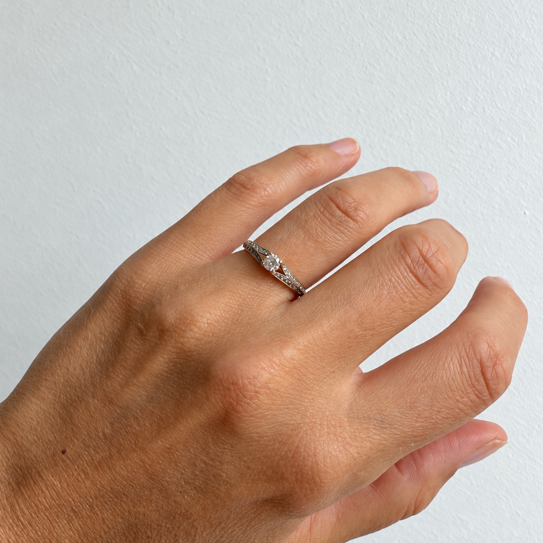 Bague solitaire en or jaune 18 carats sertie d’un diamant central entouré de deux lignes de diamants, portée au doigt.