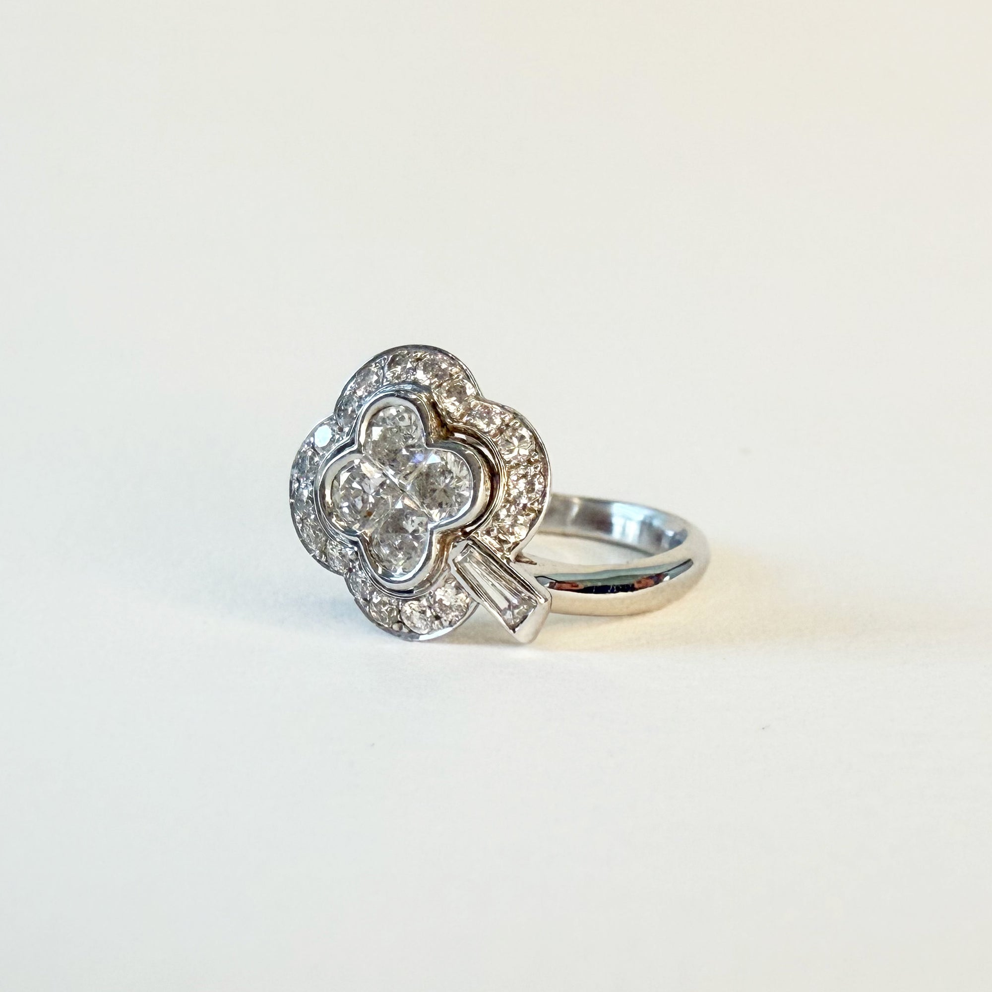 Bague en or blanc 18 carats ornée d’un motif de trèfle à quatre feuilles serti de diamants, le centre composé de quatre diamants taille princesse dans un entourage polylobé étincelant.