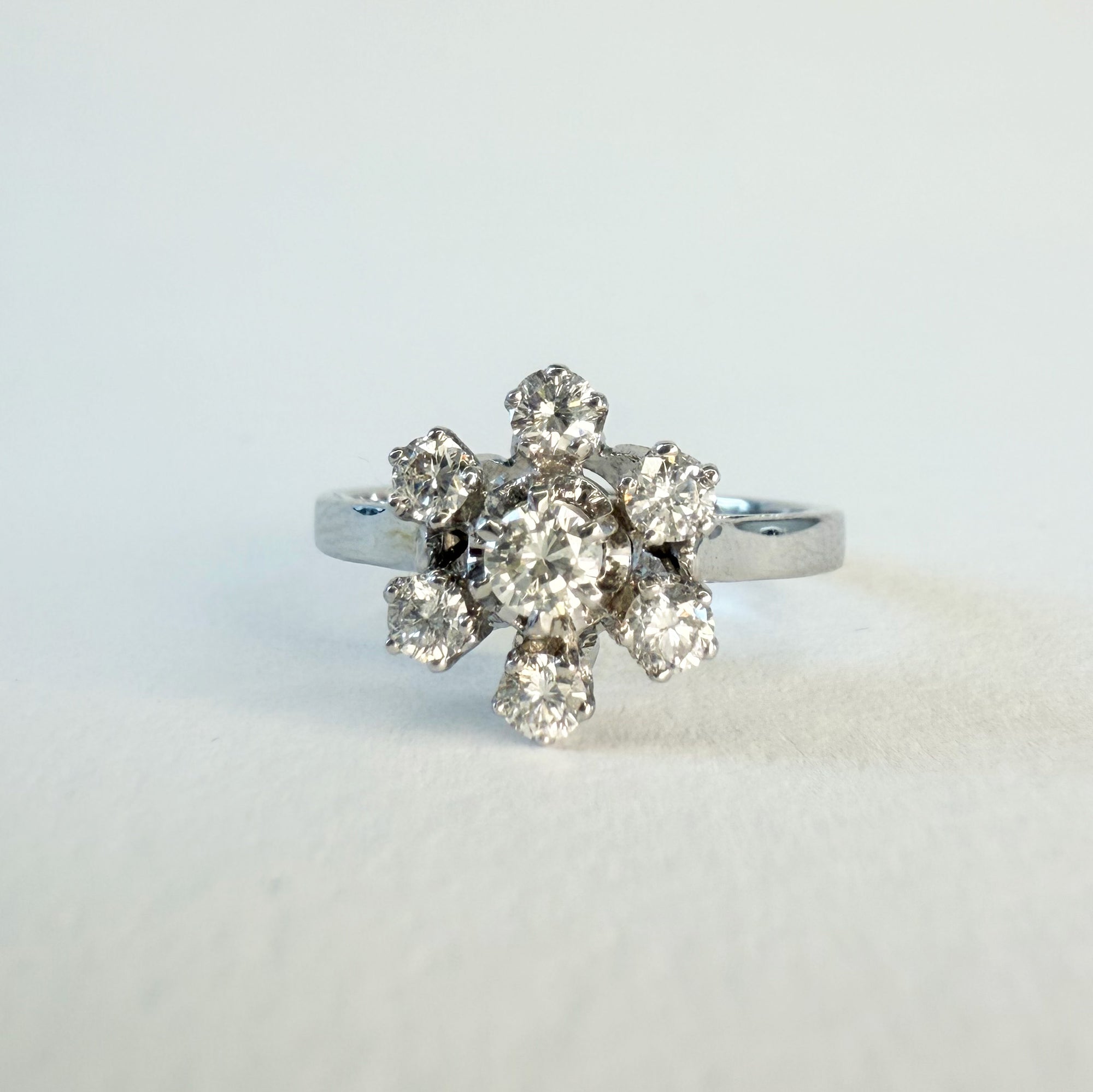 Bague en or gris 18 carats sertie de sept diamants taille brillant en serti griffe formant une fleur sur une monture ajourée, bijou raffiné et lumineux.