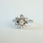 Bague en or gris 18 carats sertie de sept diamants taille brillant en serti griffe formant une fleur sur une monture ajourée, bijou raffiné et lumineux.