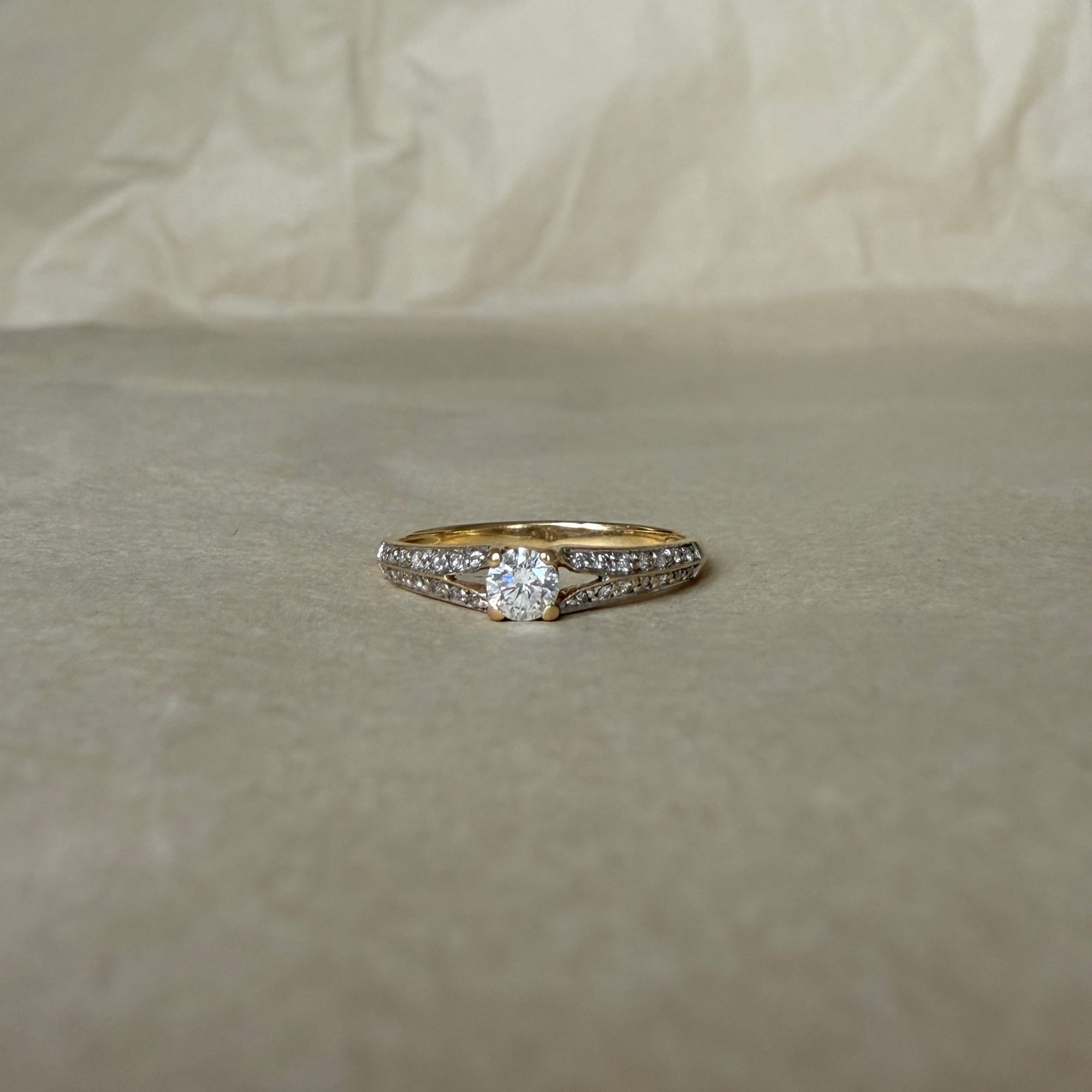 Bague solitaire en or jaune 18 carats, avec diamant central taille brillant entouré de deux rangées de petits diamants.