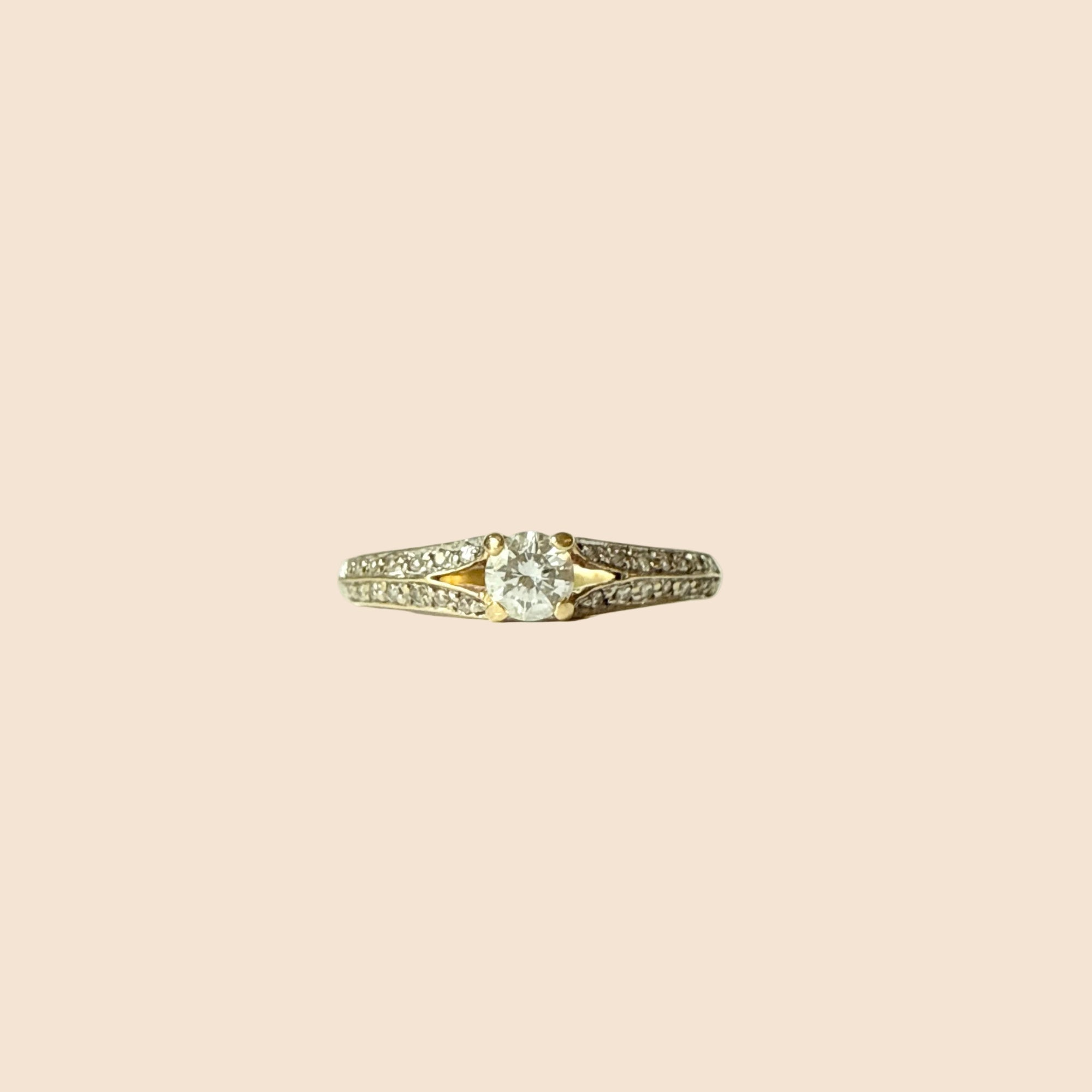 Bague solitaire en or jaune 18 carats ornée d’un diamant taille brillant de 0,20 carat entouré de deux lignes de petits diamants.