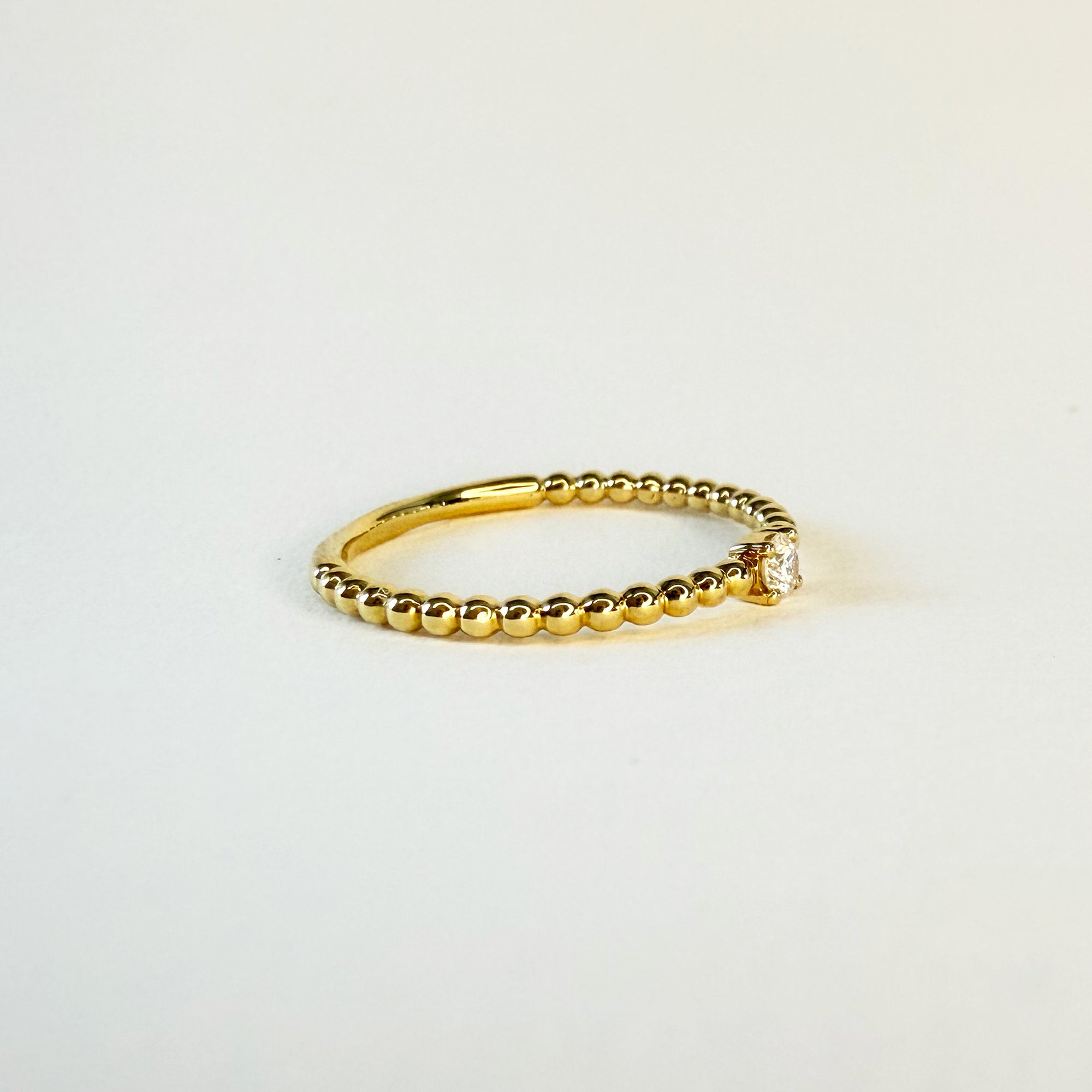 Bague solitaire en or jaune 18 carats ornée d’un diamant en serti griffe sur un anneau perlé, bijou raffiné symbolisant l’unicité et l’élégance intemporelle.