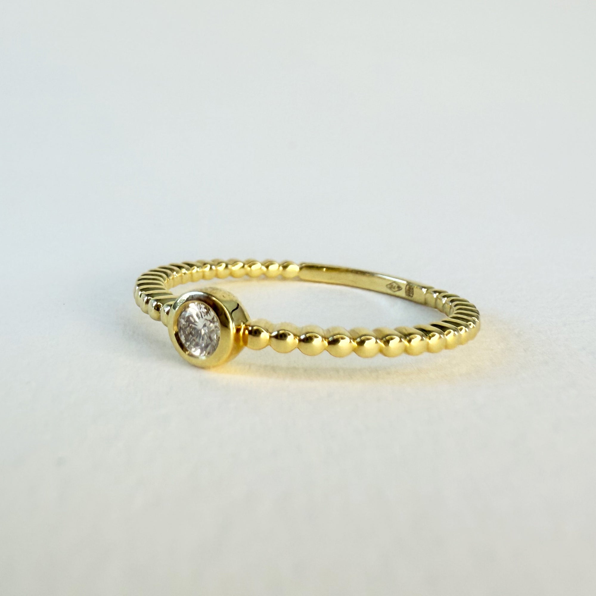 Bague solitaire en or jaune 18 carats ornée d’un diamant en serti clos sur anneau perlé, bijou raffiné symbolisant l’amour unique et éternel