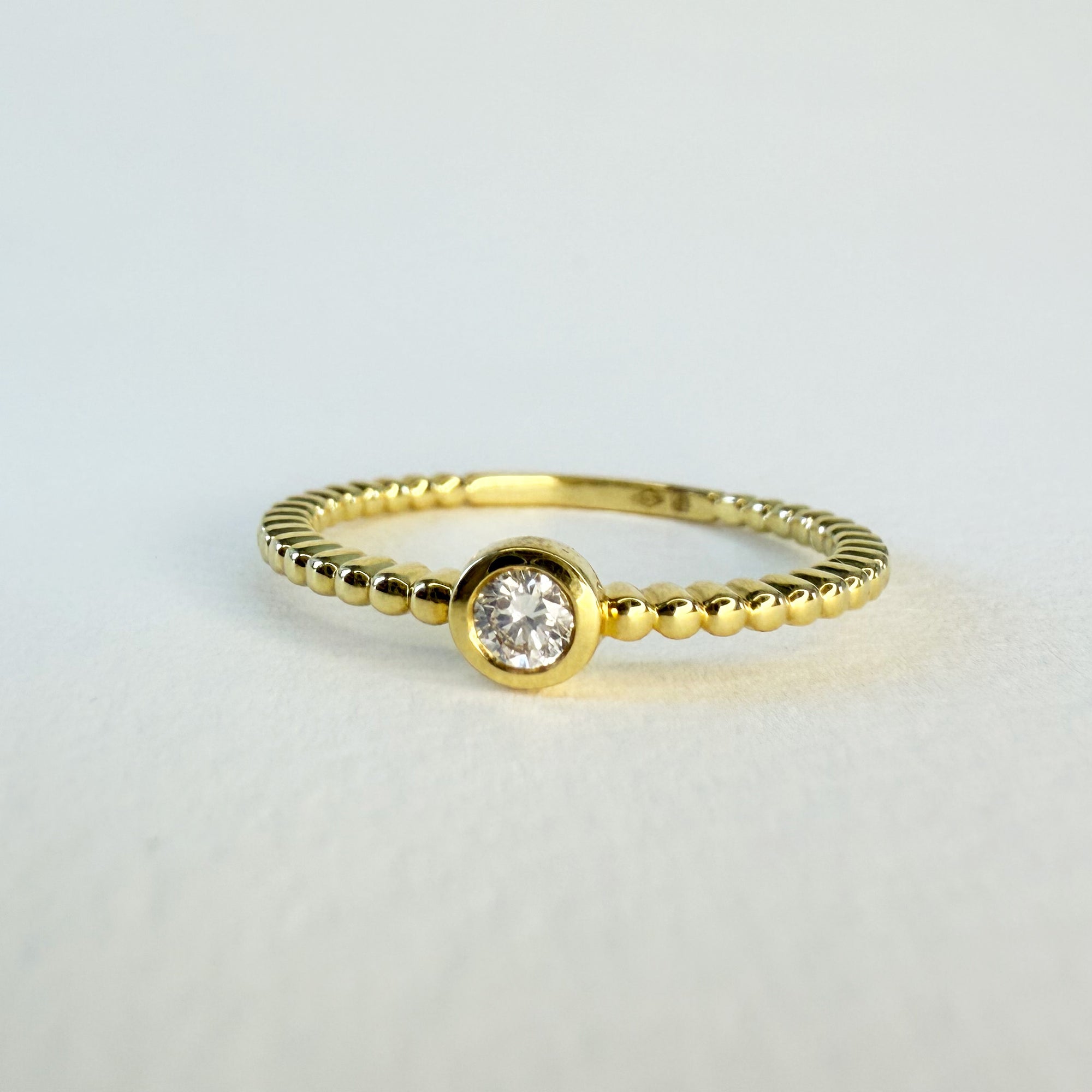 Bague solitaire en or jaune 18 carats ornée d’un diamant en serti clos sur anneau perlé, bijou raffiné symbolisant l’amour unique et éternel.