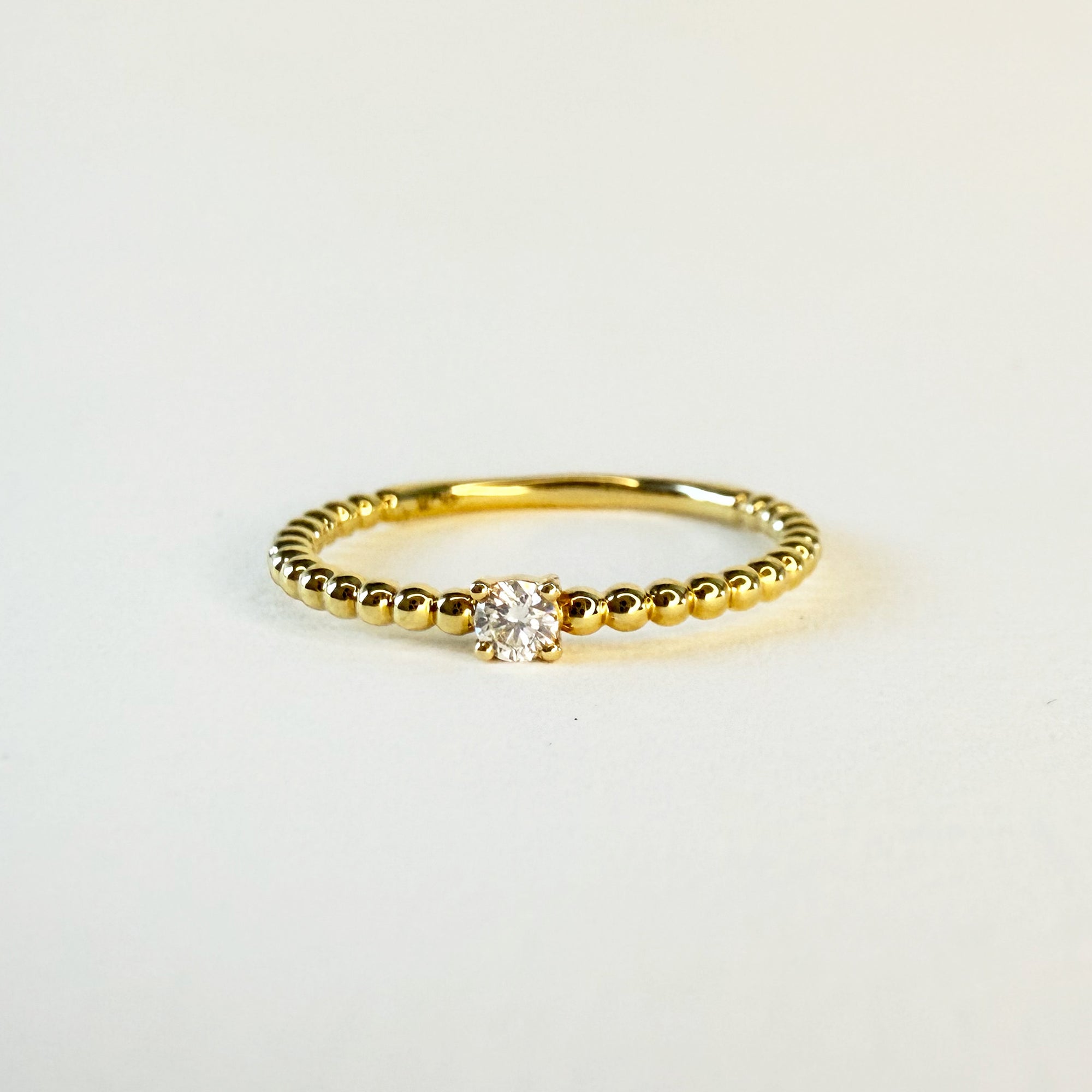 Bague solitaire en or jaune 18 carats ornée d’un diamant en serti griffe sur un anneau perlé, bijou raffiné symbolisant l’unicité et l’élégance intemporelle.