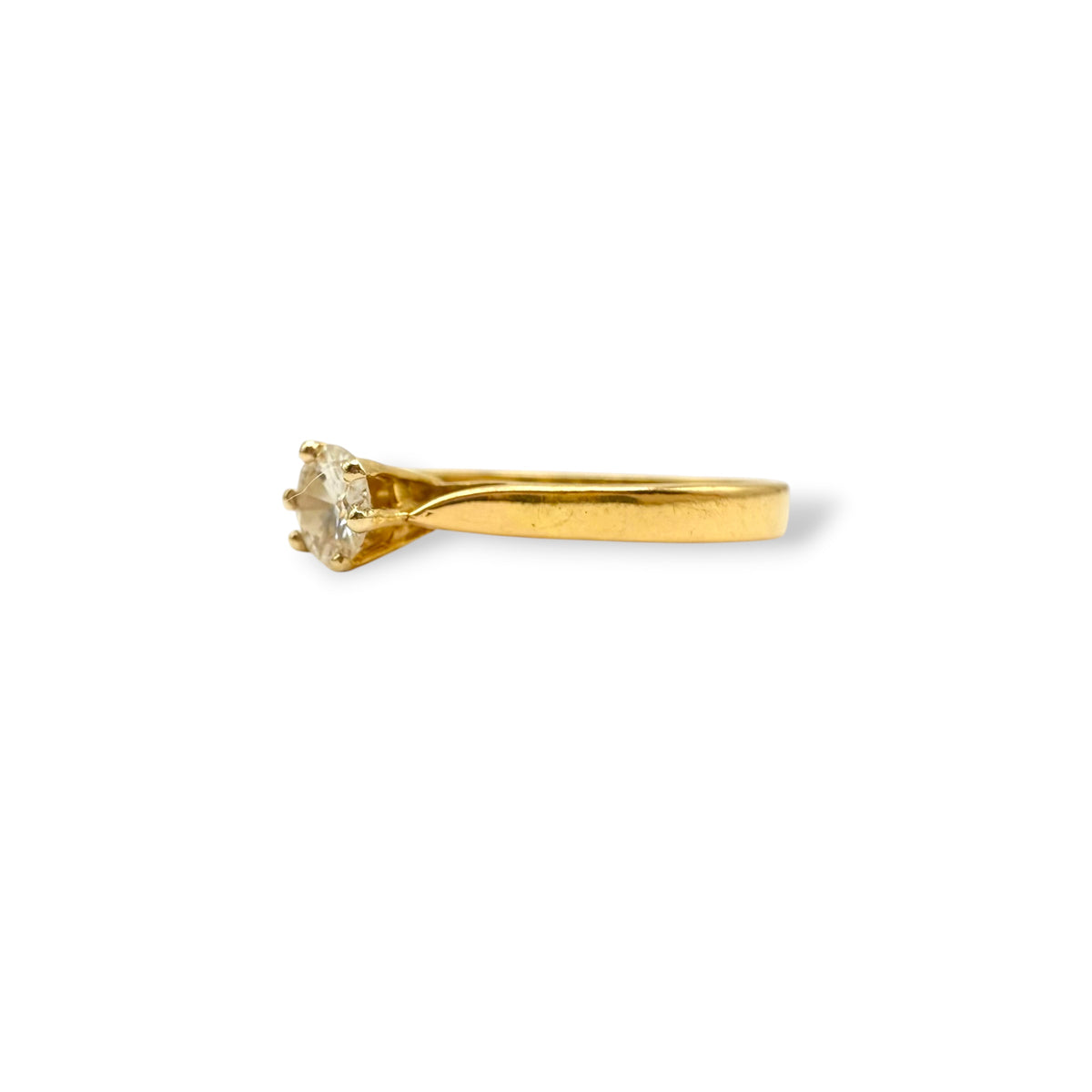 Détail du serti griffes d’une bague solitaire en or jaune 18 carats, mettant en valeur un diamant taille brillant.