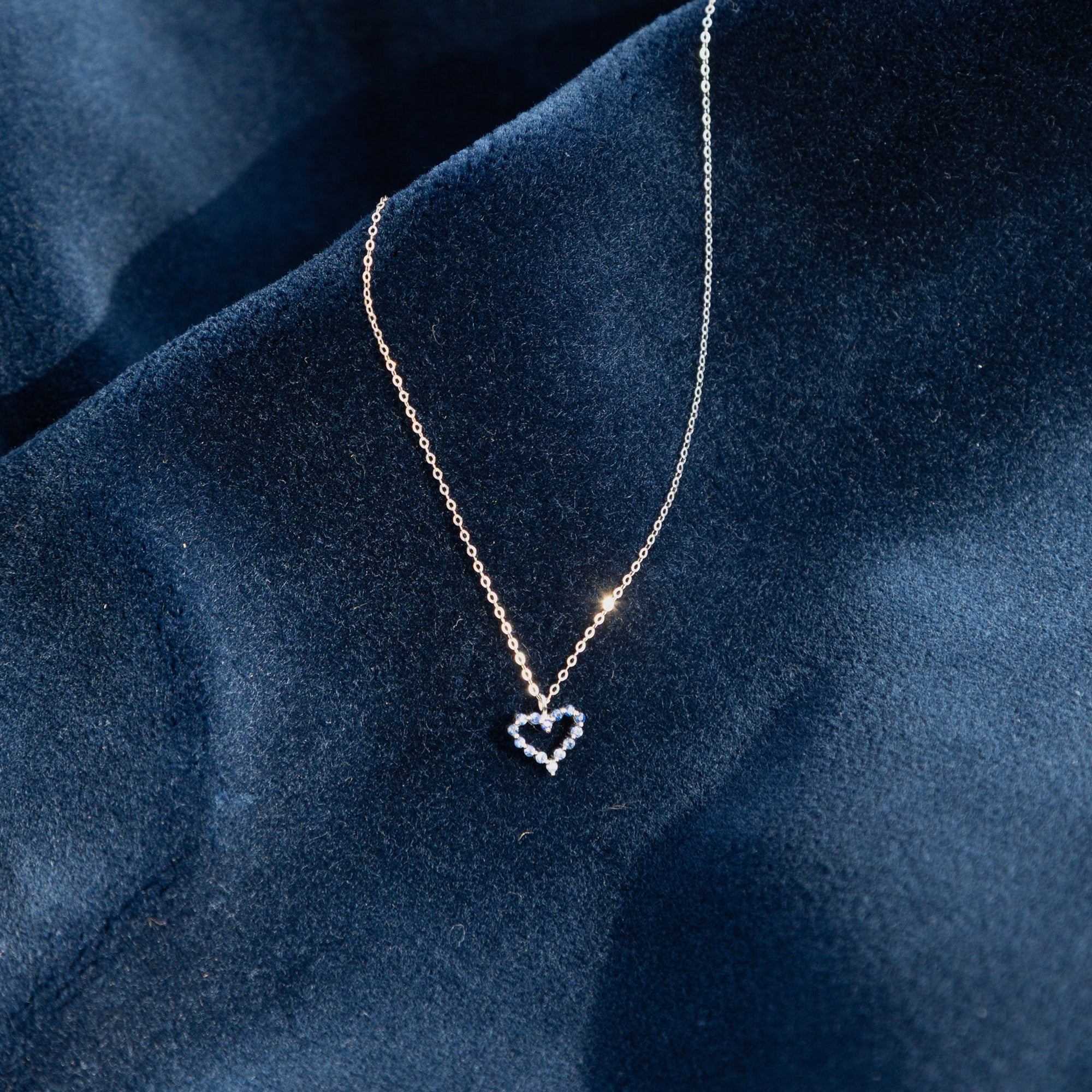 Collier pendentif cœur ajouré en or blanc 18 carats, serti de saphirs bleus ronds, chaîne fine assortie, bijou moderne et unique.