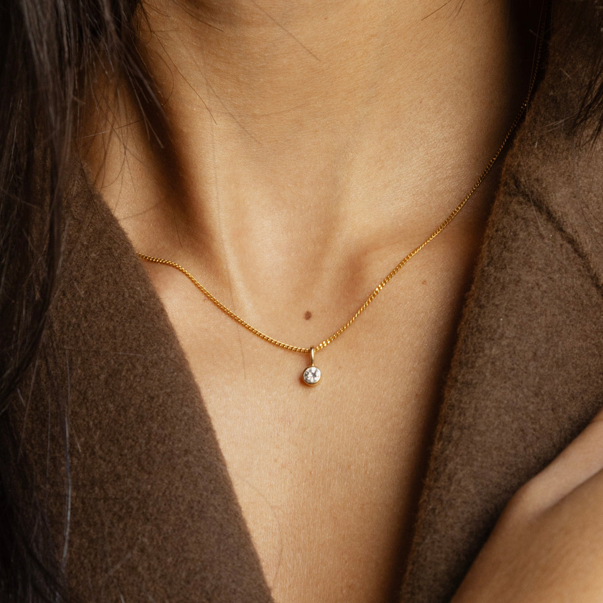 Pendentif diamant de 0.1 carat sur une chaine en or jaune 18 carats maille gourmette, porté autour du cou.