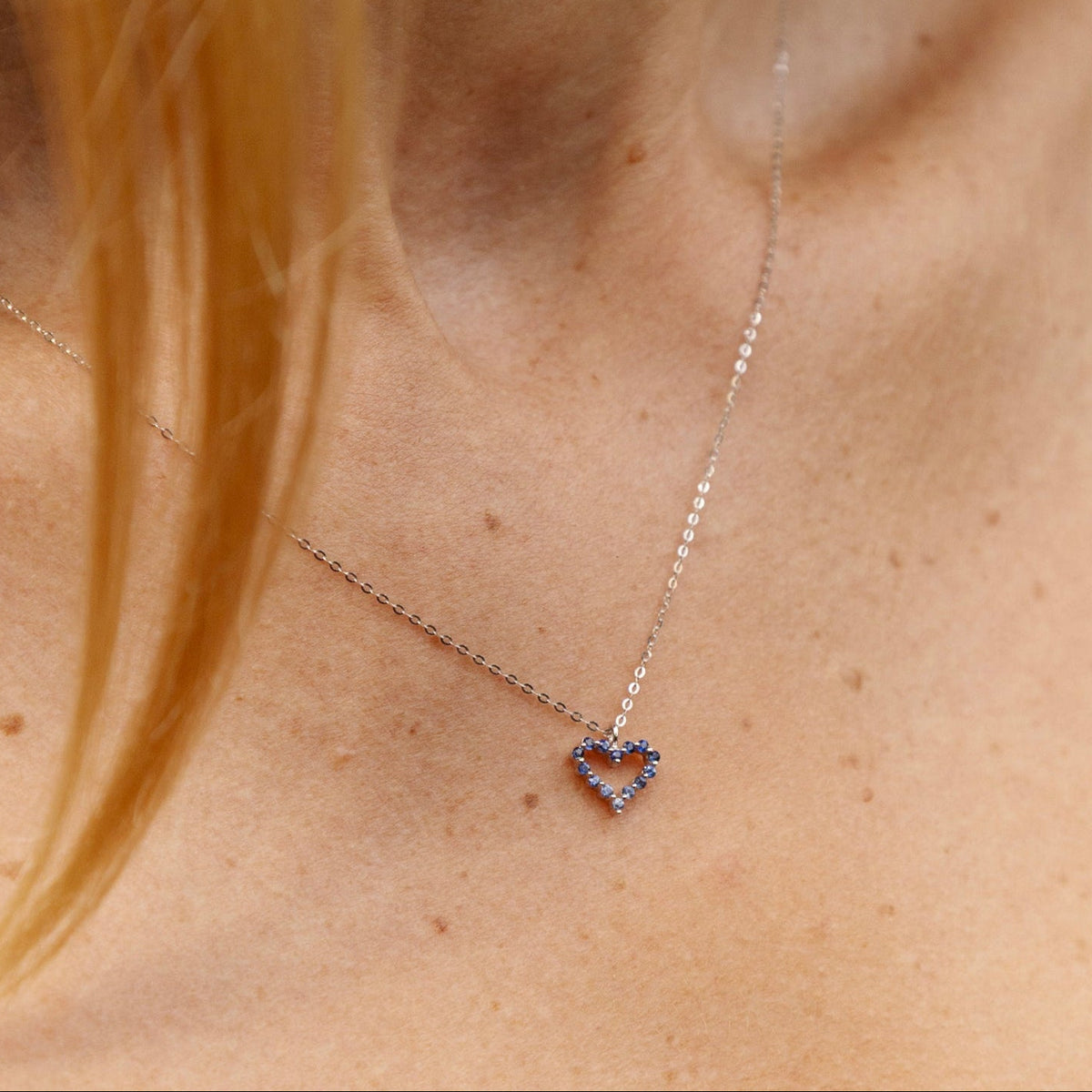 Collier pendentif cœur ajouré en or blanc 18 carats, serti de saphirs bleus ronds, chaîne fine assortie, bijou moderne et unique.