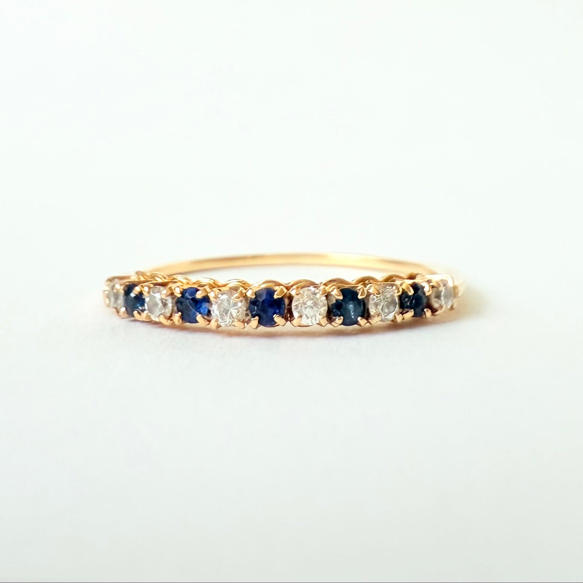 Détail du serti griffe des diamants et saphirs sur une bague demi-alliance en or jaune 18 carats