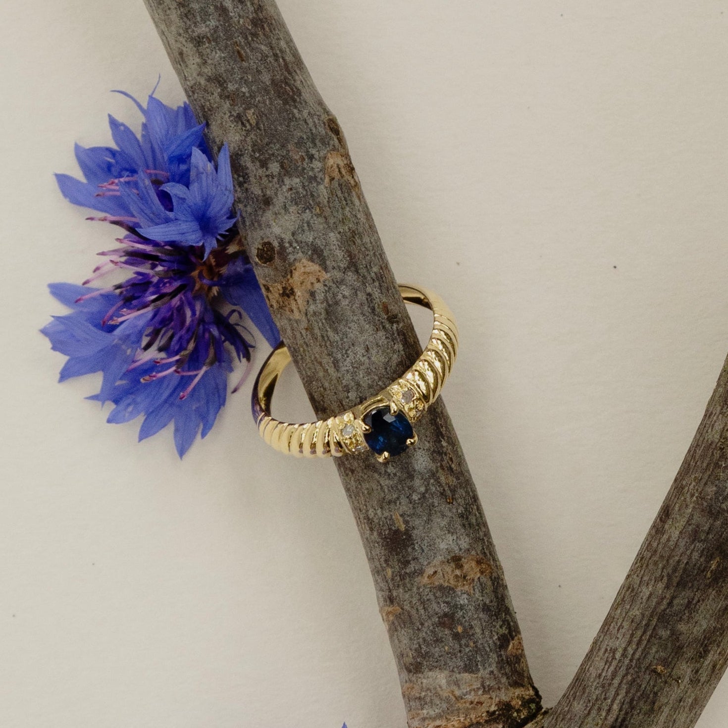 Bague en or jaune 18 carats ornée d’un saphir ovale épaulé de quatre diamants taillés en rose, monture godronnée élégante et intemporelle, bijou raffiné et lumineux.