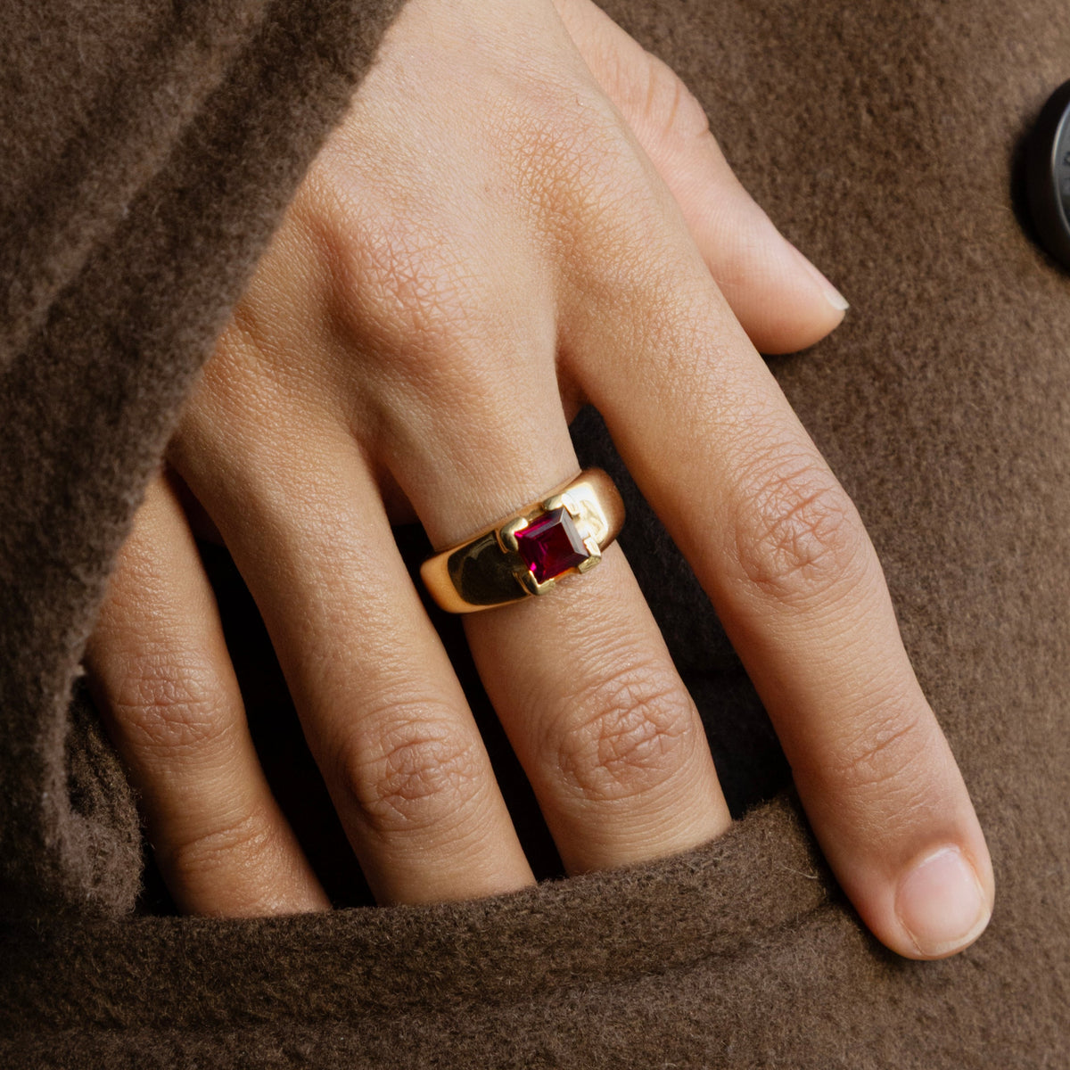 Bague bandeau de style chevalière en or jaune 18 carat ornée d'une tourmaline carré rouge-violet, montré au doigt d'une femme.