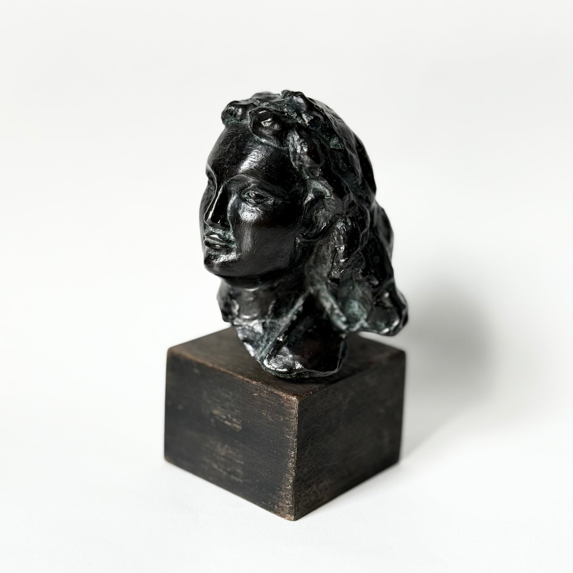Sculpture en bronze représentant un portrait de femme, tête sculptée aux traits doux et expressifs, patine sombre nuancée, reposant sur un socle en bois, œuvre du sculpteur français Maurice Guillaume (1920–2015).