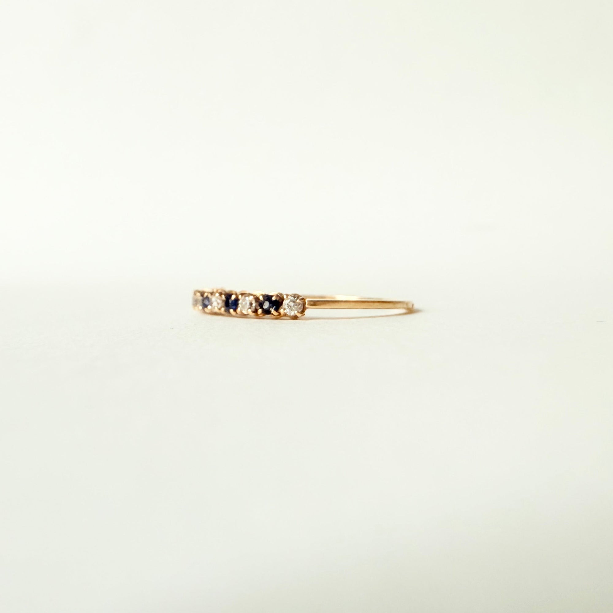 Vue de profil d’une fine bague demi-alliance en or jaune 18 carats sertie de diamants et saphirs