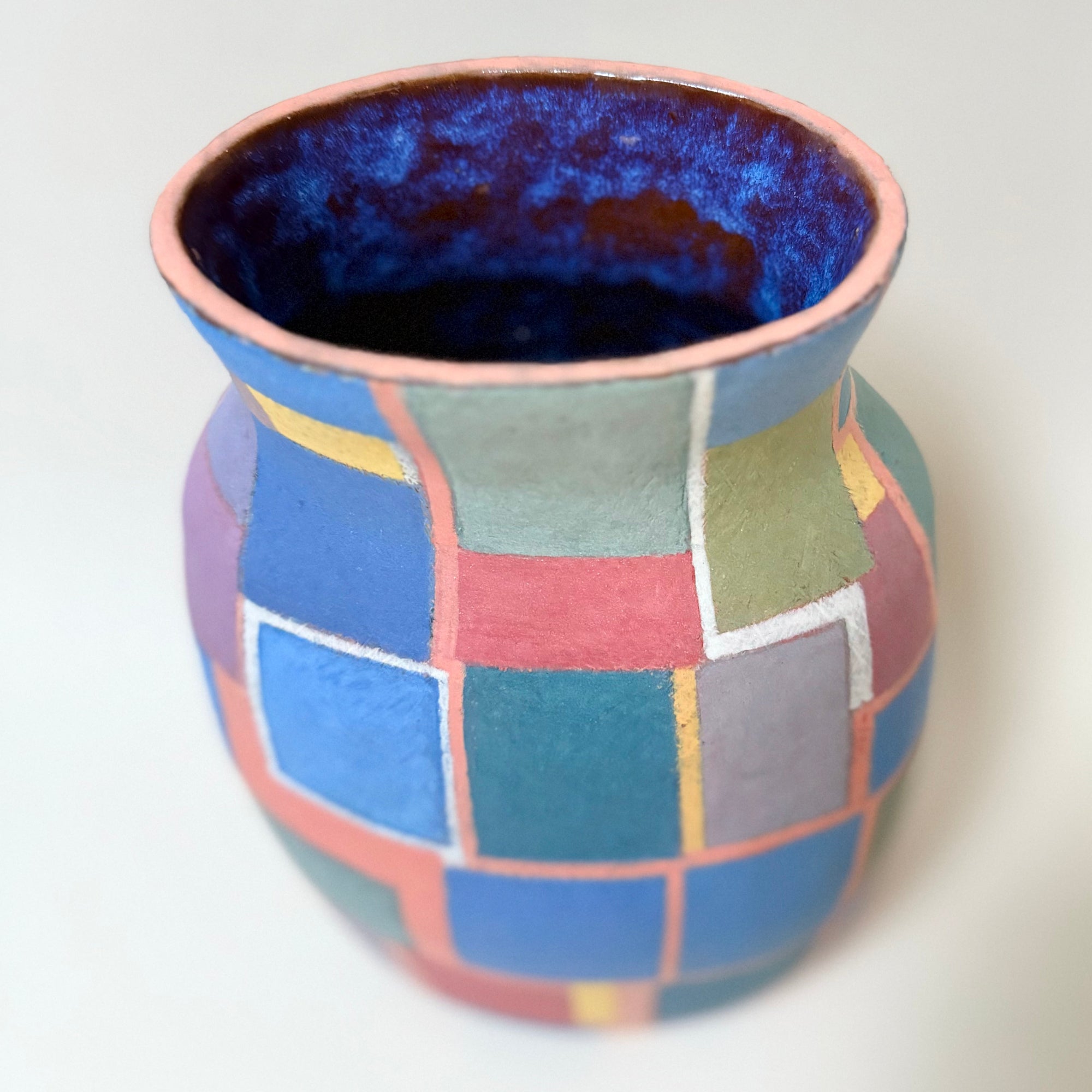 Détail du décor géométrique en cubes bleus, verts et jaunes sur fond rose pastel d’un vase vintage des années 1970